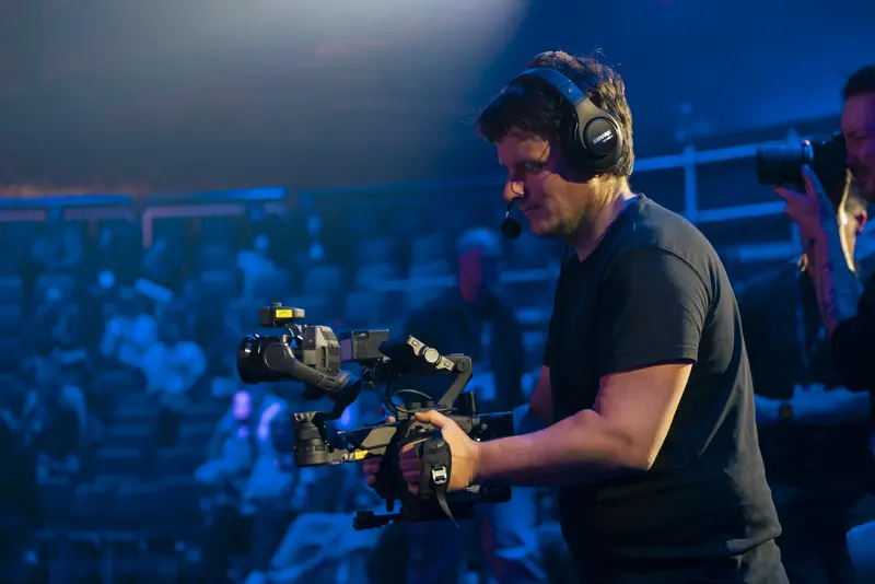 Christian Scheunert mit Gimbal-Kamera am Bühnenrand, im Hintergrund Publikum im blauen Licht