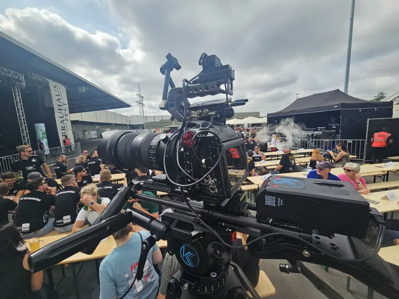Kamera mit Teleobjektiv vor einer Open-Air-Bühne mit Publikum