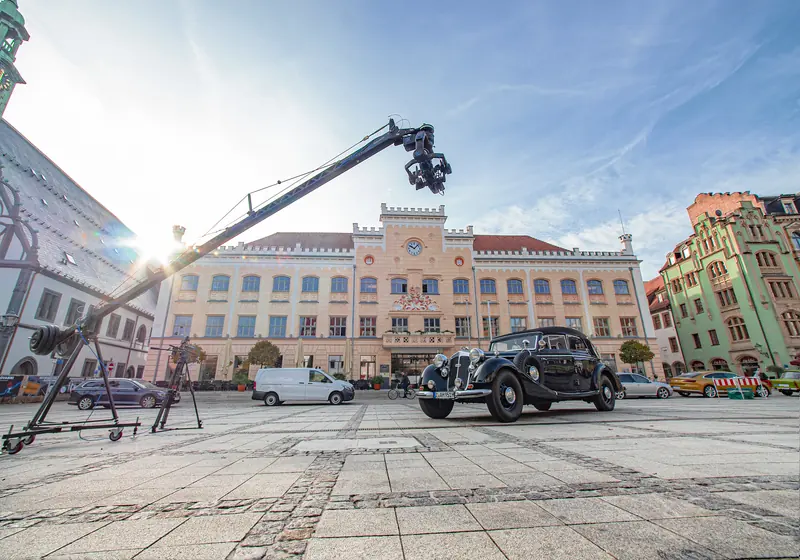 Kamerakran auf einem Platz vor einem historischen Gebäude mit Oldtimer