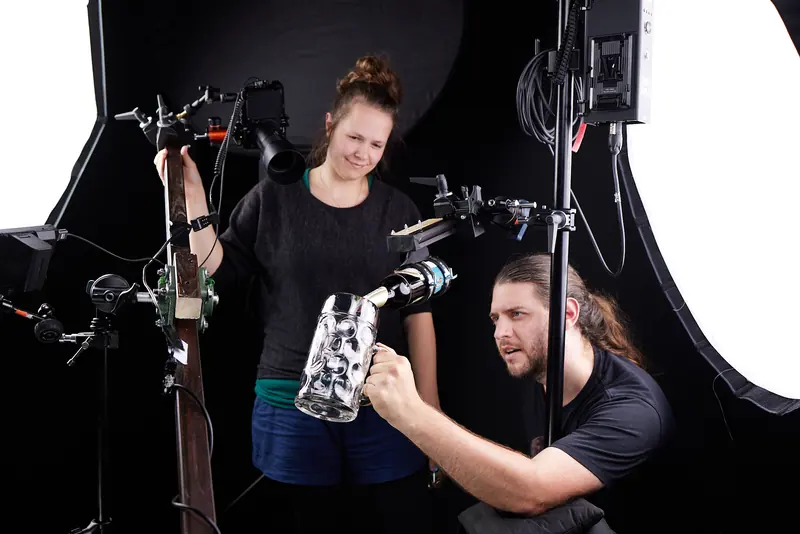Sabine Siems und ein befreundeter Beleuchter richten im Studio einen Glaskrug für einen Tabletop-Dreh ein